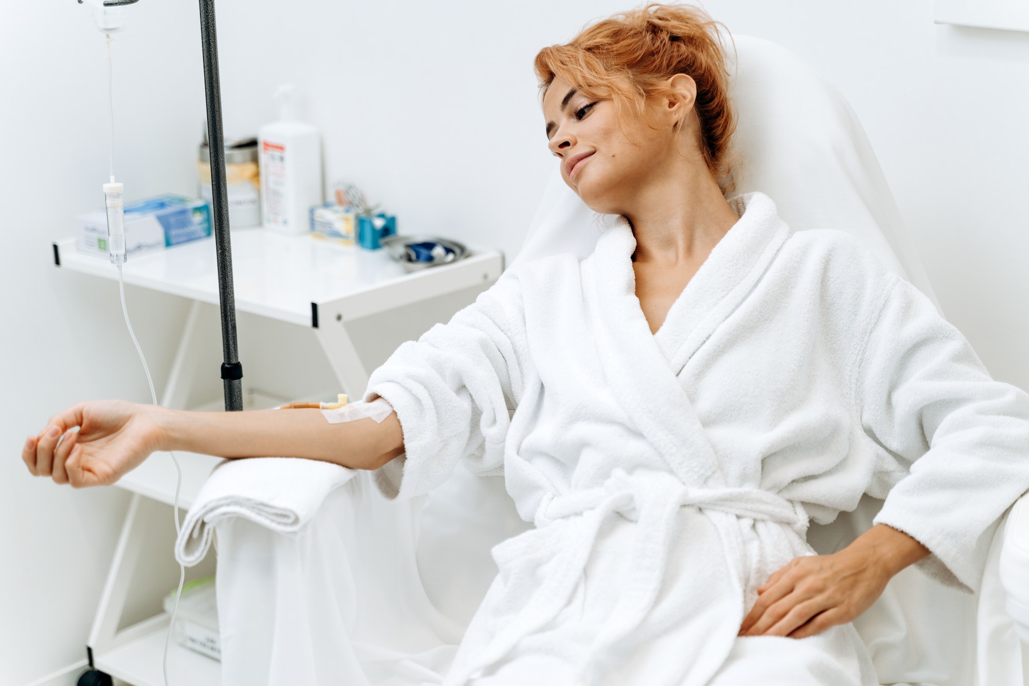 Portrait of woman sitting in armchair and closed eyes while receiving IV infusion with vitamins